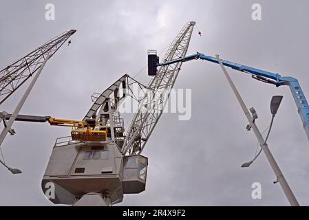 Leute auf Kirschpflückern restaurieren und streichen einen historischen Hafenkran im Hafen von Genua, Italien. Mai 2023 Stockfoto