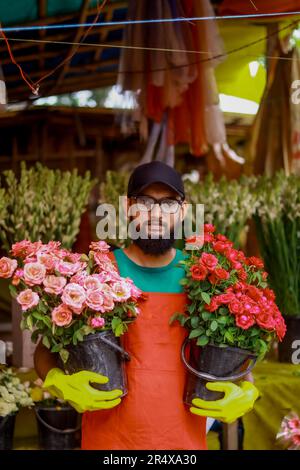 Arbeiter im Blumenladen, Porträt eines wunderschönen Mannes, der während der Arbeit in einem Gewächshaus steht, lächelnd erfolgreiche junge Pflanze. Stockfoto