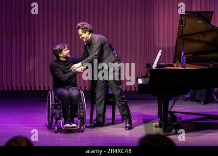 Nach einer Aufführung schüttelt ein körperlicher Konzertpianist die Hand mit einem anderen Pianisten im Rollstuhl, der eine Rückenmarksverletzung hat Stockfoto
