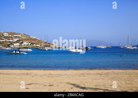 Ornos in Mykonos, Griechenland, ist eine kleine Küstenstadt mit vielen kleinen Buchten, Luxusbooten und Yachten liegen auf dem hellblauen, ruhigen Meer vor. Stockfoto