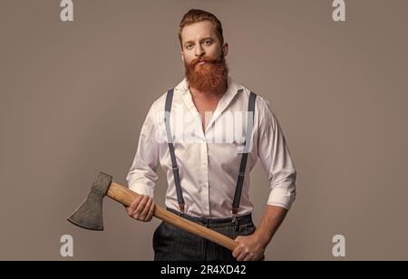 Brutaler Mann mit Axt isoliert auf grau. Brutaler Mann mit Axt im Studio. Brutaler Mann mit Axt im Hintergrund. Foto eines brutalen Mannes mit Axt. Stockfoto