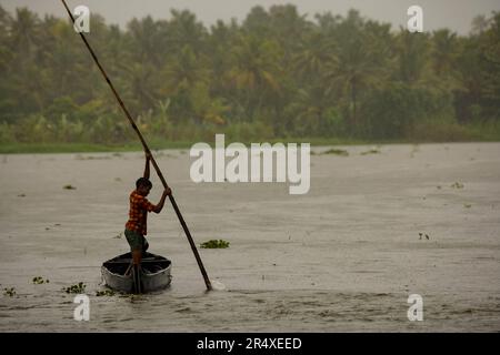 Junger Mann stemmt ein Kanu einen Fluss hinunter im Regen; Kerala State, Indien Stockfoto