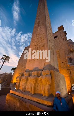 Der Mensch steht neben einem beleuchteten Obelisken im Luxor-Tempel, Luxor, Ägypten Stockfoto