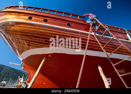 Flacher Blick auf ein türkisches Fischerboot im Trockendock mit Mann auf der Leiter; Bodrum, Republik Turkiye Stockfoto