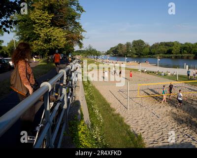 Frau, die ein Beachvolleyballspiel entlang des Flusses Odra in der Nähe der Technischen Universität, Breslau, Polen, ansieht © Renzo Frontoni / Axiom Stockfoto