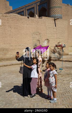 Lokale Touristen machen Fotos mit Kamel in Itchan Kala, UNESCO-Weltkulturerbe in Chiwa, Usbekistan; Chiwa, Usbekistan Stockfoto