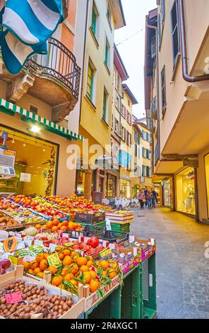 Der kleine Obststand mit frischen Orangen, Äpfeln, Kiwies, Granatäpfeln und anderen Früchten vor der engen Via Pessina, Lugano, Schweiz Stockfoto