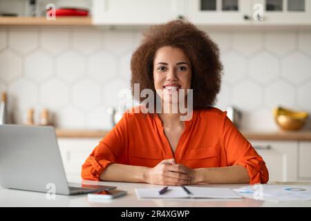 Erfolgreicher Freiberufler. Glückliche Schwarze Frau Sitzt Am Schreibtisch Mit Computer In Der Küche Stockfoto
