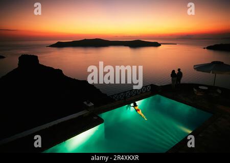 Ein Paar und eine Frau in einem Pool, die einen malerischen Sonnenuntergang beobachten; Santorin, Griechenland Stockfoto