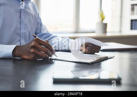 Nahaufnahme eines schwarzen Geschäftsmanns, der ein Dokument am Schreibtisch im Büro unterschreibt, Kopierraum Stockfoto