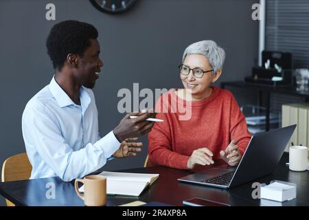 Porträt einer lächelnden Geschäftsfrau, die mit einem Kollegen am Schreibtisch arbeitet Stockfoto