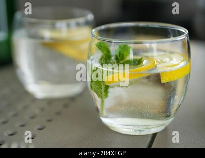 Ein Glas Wasser mit einer Scheibe Zitrone und Minze auf einem Tisch in einem Restaurant. Nahaufnahme eines erfrischenden, gekühlten Getränks. Zitronensaft, Zitronensaft, Stockfoto