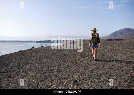 Eine Frau, die auf einer Klippe spaziert und den Sonnenuntergang über dem Meer sieht. Reisen und Tourismus. Stockfoto