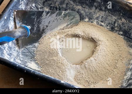 Zementpulver mit Wasser, fertig zur Mischung mit einer Kelle in einer Kunststoffschüssel, Mörtelherstellung. Stockfoto