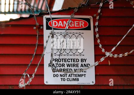 Ein Schild mit der Aufschrift „Gefahr, geschützt durch Rasierdraht und Stacheldraht, nicht versuchen zu klettern“, umgeben von Rasierdraht, an einem Schaufenster in New York City Stockfoto