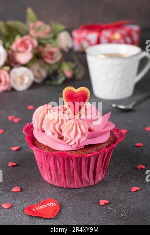 Roter Samt-Cupcake mit pinkfarbener Creme und einem Keksherz sowie als Tasse Kaffee Stockfoto