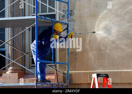 Ein Arbeiter wäscht Graffiti und Dreck mit einer Hochdrucksprühpistole von einem Schulgebäude in New York City. Stockfoto