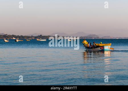 Ein Boot mit mehreren Fischern nähert sich dem kleinen Fischerhafen von Makawa am Malawi-See nahe Mangochi, mehrere Boote liegen vor der Küste vor Anker. Stockfoto