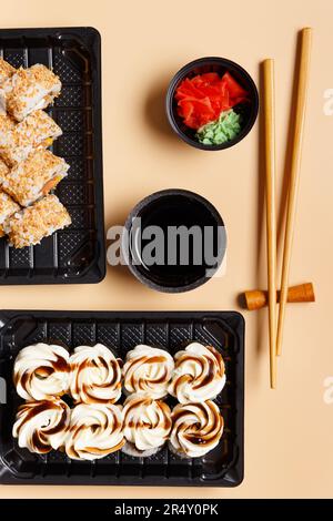 Ein Set Sushi-Brötchen in Plastikpackungen zum Mitnehmen mit Sojasoße, Ingwer, Wasabi und chinesischen Essstäbchen auf hellem Hintergrund, Draufsicht. Lieferung Stockfoto