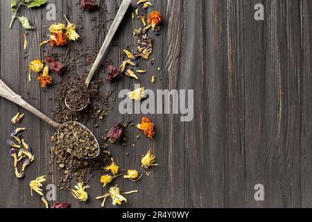 Zusammensetzung von trockenem Schwarz- und Grüntee in klassischen Löffeln, trockenem Blumentee auf dunklem Holzhintergrund, Draufsicht mit Platz für Text. Stockfoto