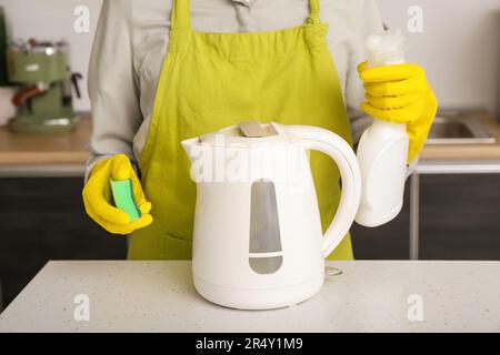 Frau in gelben Handschuhen, die elektrischen Wasserkocher auf einem weißen Tisch reinigt Stockfoto