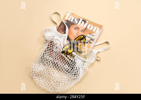 Stilvolle Sonnenbrille und Tragetasche mit Zeitschrift auf beigefarbenem Hintergrund Stockfoto
