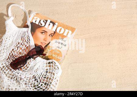 Stilvolle Sonnenbrille und Tragetasche mit Magazin auf Sand Stockfoto