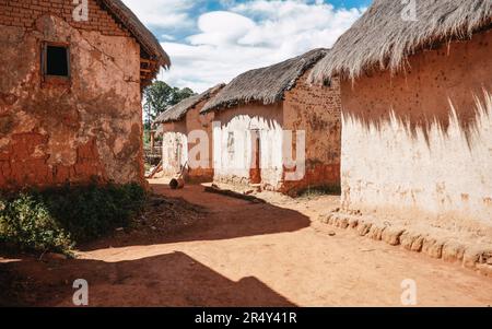 Einfache rote Tonhäuser mit Strohdach an sonnigen Tagen - typische Architektur in kleineren Dörfern Madagaskars Stockfoto