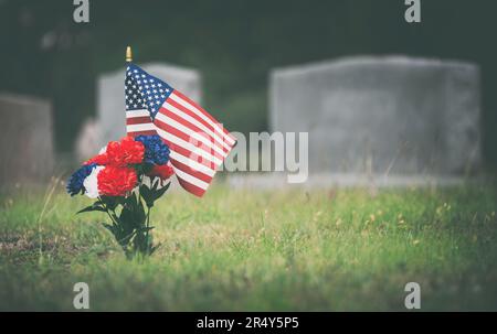 Amerikanische Flagge und rote, weiße und blaue Blumen auf dem Grab des Veteranen. Zu Ehren eines gefallenen Soldaten auf dem Friedhof am Memorial Day. Stockfoto