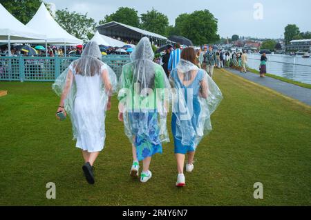 Drei junge Frauen halten den Regen mit transparenten Parkas im Regatta-Gehege in Henley Royal Regatta, Henley-on-Thames, 2022, ab Stockfoto