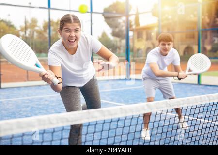 Emotionale männliche und weibliche Tennispartner, die im Sommer mit Schlägern auf Hartplätzen spielen Stockfoto