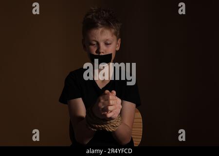 Ein kleiner Junge mit gefesseltem Mund, der vor dunklem Hintergrund als Geisel genommen wurde Stockfoto