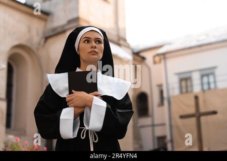 Junge Nonne mit Bibel in der Nähe von Gebäuden im Freien, Platz für Text Stockfoto