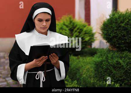 Junge Nonne liest Bibel in der Nähe von Gebäuden im Freien Stockfoto
