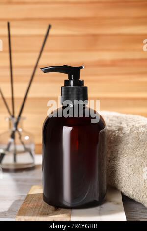 Eine Flasche Shampoo und ein gerolltes Handtuch auf einem weißen Tisch nahe der Holzwand, Nahaufnahme Stockfoto