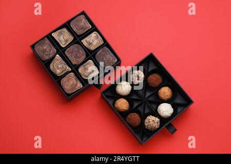 Schachteln mit leckeren Schokoladenbonbons auf rotem Hintergrund, flach liegend Stockfoto