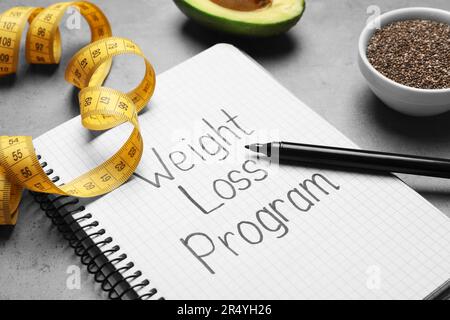 Notizbuch mit Phrase Weight Loss Program, Maßband, Chiasamen und Avocado auf grauem Tisch, Nahaufnahme Stockfoto