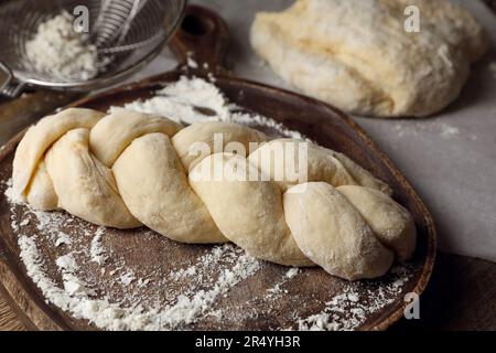 Rohes geflochtenes Brot und Mehl auf Holztisch, Nahaufnahme. Traditionelle Sabbat-Challah Stockfoto