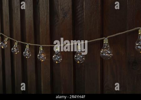 Girlande aus Lampen, die an der Holzwand hängen. Lichterkette Stockfoto