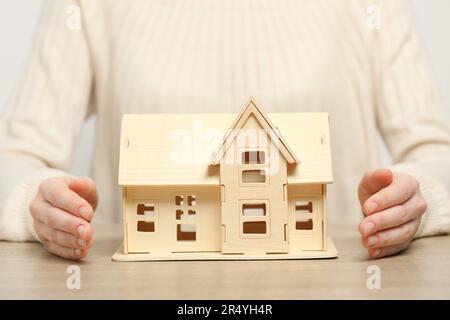 Heimsicherheitskonzept. Frau mit Hausmodell am Holztisch, Nahaufnahme Stockfoto