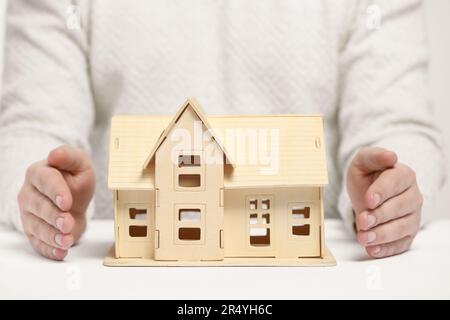 Heimsicherheitskonzept. Mann mit Hausmodell am weißen Tisch, Nahaufnahme Stockfoto