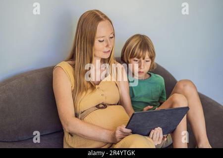 Schwangere mutter und Sohn sehen sich die Tablette an. Ein Buch lesen, einen Cartoon ansehen oder einen Videoanruf tätigen. Sehen Sie sich das Foto vom Ultraschall an Stockfoto