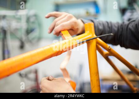 Nicht wiedererkennbare Person, die den Rahmen eines Fahrrads für die Lackierung vorbereitet, die Farbe ändert, in seiner Reparaturwerkstatt. Selektive Fokuszusammensetzung. Stockfoto