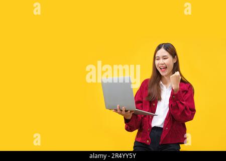 Frauen halten Laptop und heben den Arm, um mit leerem Platz auf isoliertem gelben Hintergrund zu feiern. Stockfoto