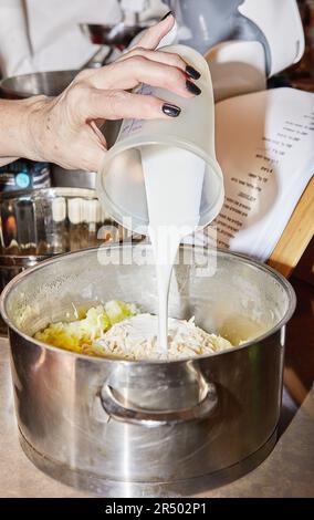 Der Küchenchef in der Küche gießt Milch aus dem Messglas mit Zutaten in den Topf Stockfoto