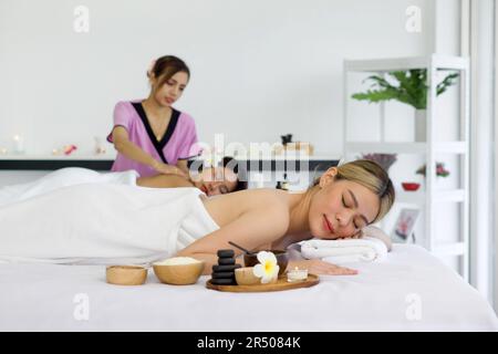 Junge asiatische Frau, die sich glücklich fühlt und sich während der Massage entspannt. Attraktives, wunderschönes Mädchen, das auf dem Massagetisch liegt und Physiotherapie von der Masseurin für sk bekommt Stockfoto