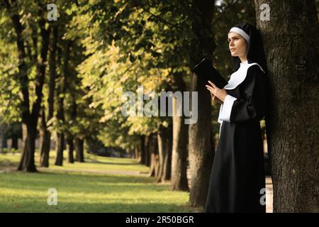Junge Nonne, die an sonnigen Tagen im Park Bibel liest, Platz für Text Stockfoto