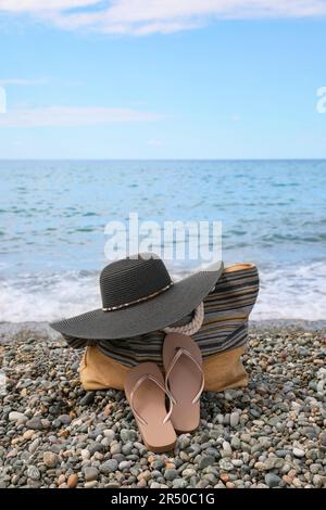 Wunderschöne Mütze, Tasche und Flip Flops nahe dem Meer am Kieselstrand Stockfoto