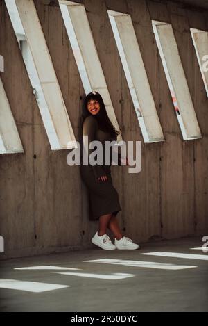 Eine selbstbewusste und stilvolle Frau in Übergröße, die sich vor einem modernen Gebäude in einem olivgrünen Kleid posiert, das Schönheit, Befähigung und Selbstliebe ausstrahlt. Stockfoto