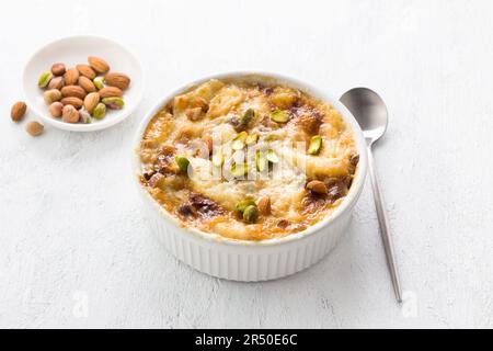 Traditionelles arabisches Dessert Umm Ali in weißer Keramikform, dekoriert mit Nüssen auf hellgrauem Hintergrund Stockfoto